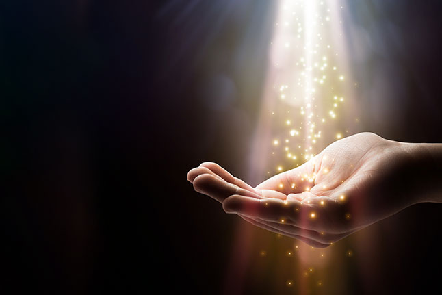 A person's hand channeling energetic healing with a glowing light emanating from it.