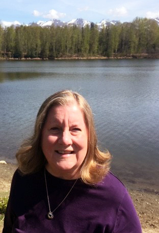 A woman standing in front of a lake with mountains in the background, embodying spiritual healing and Energetic healing energy.